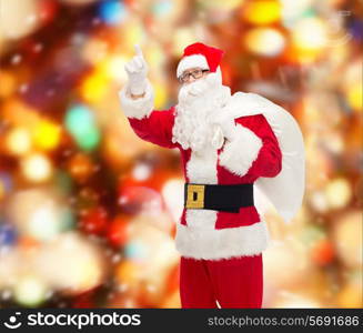 christmas, holidays, gesture and people concept - man in costume of santa claus with bag pointing finger up over red lights background