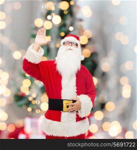 christmas, holidays, gesture and people concept - man in costume of santa claus waving hand over tree lights background
