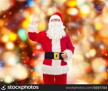 christmas, holidays, gesture and people concept - man in costume of santa claus waving hand over red lights background