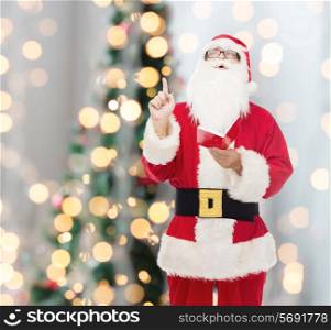 christmas, holidays, gesture and people concept - man in costume of santa claus with notepad pointing finger up over tree lights background