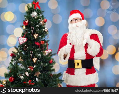 christmas, holidays, gesture and people concept - man in costume of santa claus with bag and christmas tree showing thumbs up over blue lights background