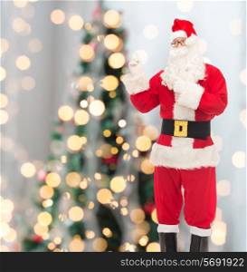 christmas, holidays, gesture and people concept - man in costume of santa claus pointing fingers over tree lights background