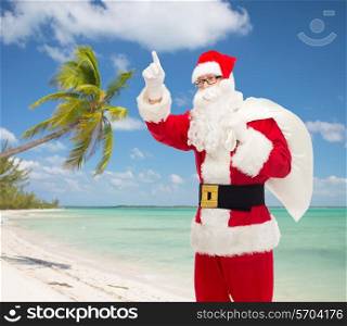 christmas, holidays, gesture and people concept - man in costume of santa claus with bag pointing finger up over tropical beach background