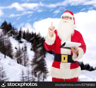 christmas, holidays, gesture and people concept - man in costume of santa claus with notepad pointing finger up over snowy mountains background