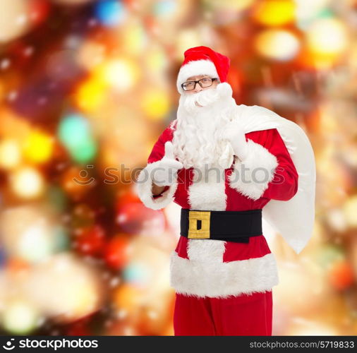 christmas, holidays, gesture and people concept - man in costume of santa claus with bag showing thumbs up over red lights background