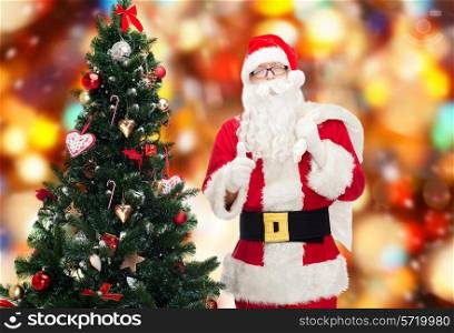 christmas, holidays, gesture and people concept - man in costume of santa claus with bag and christmas tree showing thumbs up over red lights background