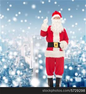 christmas, holidays, gesture and people concept - man in costume of santa claus pointing finger up over snowy city background