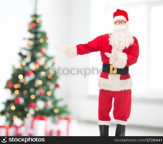 christmas, holidays, gesture and people concept - man in costume of santa claus over living room and tree background