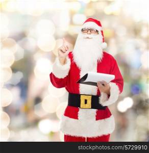 christmas, holidays, gesture and people concept - man in costume of santa claus with notepad pointing finger up over lights background