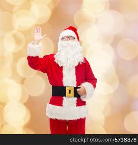 christmas, holidays, gesture and people concept - man in costume of santa claus waving hand over beige lights background