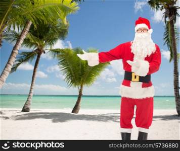 christmas, holidays, gesture and people concept - man in costume of santa claus over tropical beach background