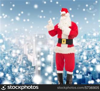 christmas, holidays, gesture and people concept - man in costume of santa claus pointing fingers over snowy city background