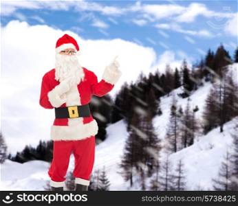 christmas, holidays, gesture and people concept - man in costume of santa claus pointing fingers over snowy mountains background