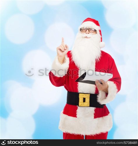 christmas, holidays, gesture and people concept - man in costume of santa claus with notepad pointing finger up over blue lights background