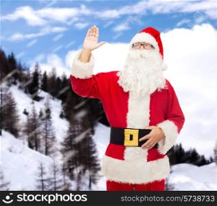 christmas, holidays, gesture and people concept - man in costume of santa claus waving hand over snowy mountains background