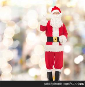 christmas, holidays, gesture and people concept - man in costume of santa claus pointing finger up over lights background