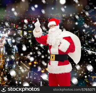 christmas, holidays, gesture and people concept - man in costume of santa claus with bag pointing finger up over snowy night city background