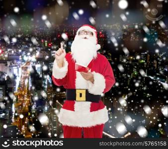 christmas, holidays, gesture and people concept - man in costume of santa claus with notepad pointing finger up over snowy night city background