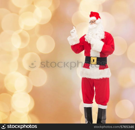 christmas, holidays, gesture and people concept - man in costume of santa claus pointing fingers over beige lights background