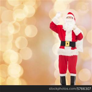 christmas, holidays, gesture and people concept - man in costume of santa claus with bag waving hand over beige lights background