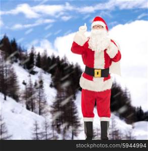 christmas, holidays, gesture and people concept - man in costume of santa claus with bag pointing finger up over snowy mountains background