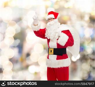 christmas, holidays, gesture and people concept - man in costume of santa claus with bag pointing finger up over lights background