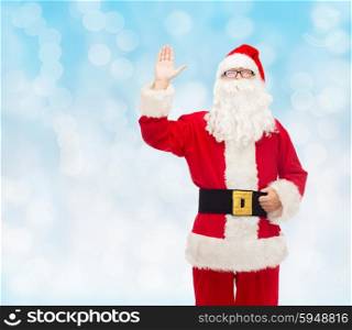 christmas, holidays, gesture and people concept - man in costume of santa claus waving hand over blue lights background