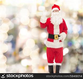christmas, holidays, gesture and people concept - man in costume of santa claus waving hand over lights background