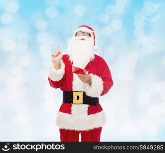 christmas, holidays, gesture and people concept - man in costume of santa claus with notepad pointing finger up over blue lights background