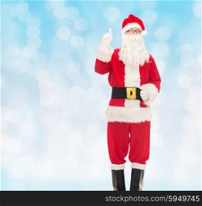 christmas, holidays, gesture and people concept - man in costume of santa claus pointing finger up over blue lights background