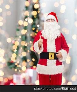 christmas, holidays, gesture and people concept- man in costume of santa claus showing thumbs up over tree lights background