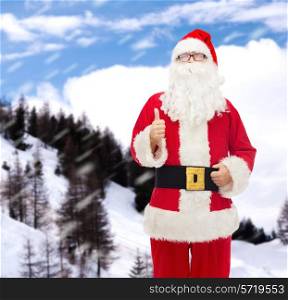 christmas, holidays, gesture and people concept- man in costume of santa claus showing thumbs up over snowy mountains background