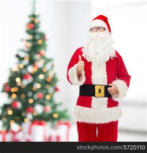 christmas, holidays, gesture and people concept- man in costume of santa claus showing thumbs up over living room with tree background