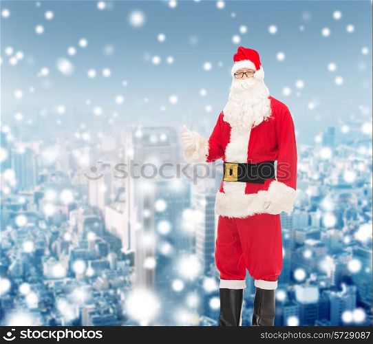 christmas, holidays, gesture and people concept- man in costume of santa claus showing thumbs up over snowy city background