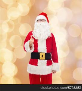 christmas, holidays, gesture and people concept- man in costume of santa claus showing thumbs up over beige lights background