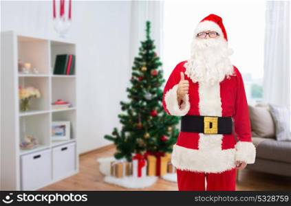 christmas, holidays, gesture and people concept- man in costume of santa claus showing thumbs up. santa claus showing thumbs up at christmas home
