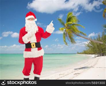 christmas, holidays, gesture, travel and people concept - man in costume of santa claus pointing fingers over tropical beach background