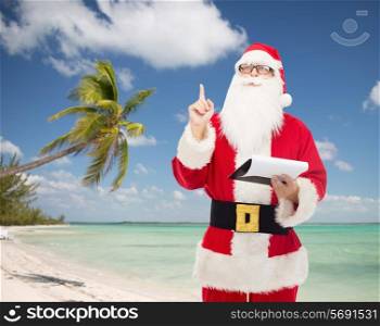 christmas, holidays, gesture, travel and people concept - man in costume of santa claus with notepad pointing finger up over tropical beach background
