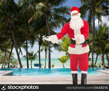 christmas, holidays, gesture, travel and people concept - man in costume of santa claus over swimming pool on tropical beach background