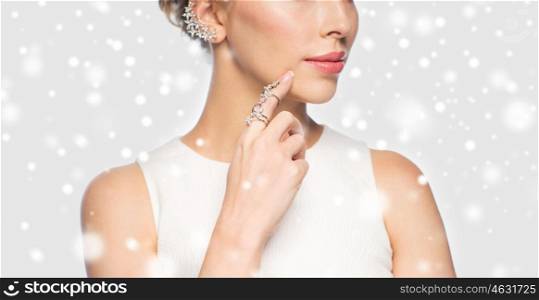 christmas, holidays, jewelry, people and luxury concept - close up of beautiful woman with golden ring and diamond earring over gray background and snow