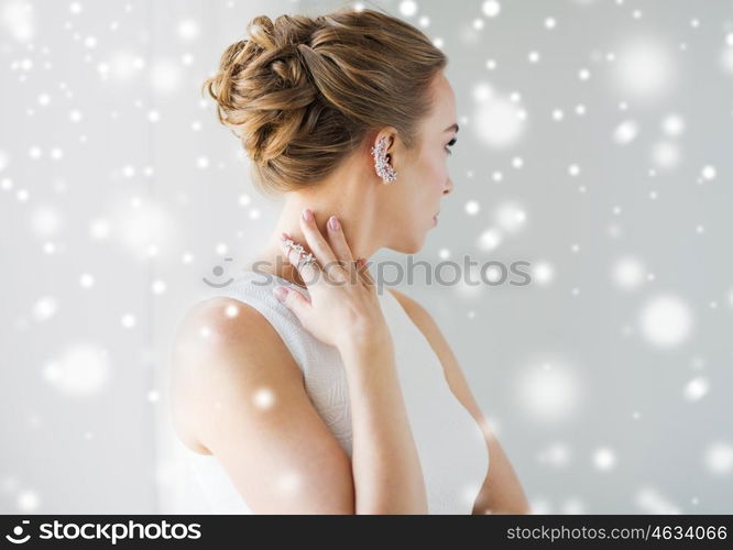 christmas, holidays, jewelry, people and luxury concept - close up of beautiful woman with golden ring and diamond earring over gray background and snow