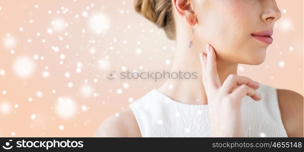 christmas, holidays, jewelry, people and luxury concept - close up of beautiful woman face with gold and diamond earring over beige background
