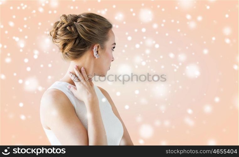 christmas, holidays, jewelry, people and luxury concept - close up of beautiful woman with golden ring and diamond earring over beige background