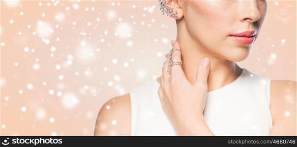 christmas, holidays, jewelry, people and luxury concept - close up of beautiful woman with golden ring and diamond earring over beige background