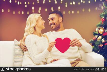 christmas, holidays, love and people concept - happy couple with red heart over lights background. happy couple with red heart at christmas