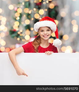 christmas, holidays, people, advertisement and sale concept - happy little girl in santa helper hat with blank white board over tree lights background