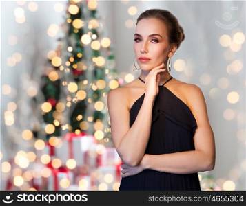 christmas, holidays, people, jewelry and luxury concept - beautiful woman in black wearing diamond earrings over lights background