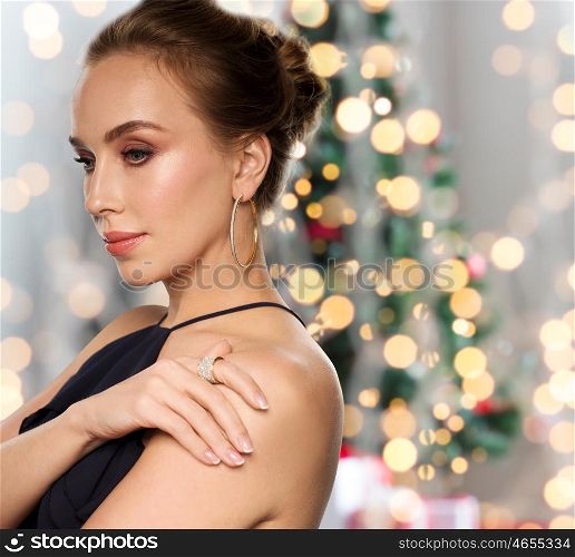 christmas, holidays, people, jewelry and luxury concept - beautiful woman in black wearing diamond earring and ring over lights background