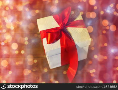 christmas, holidays, presents, new year and celebration concept - close up of gift box with red bow on wooden floor from top over lights
