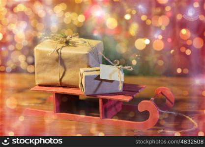 christmas, holidays, presents, new year and celebration concept - close up of gift boxes with blank note on red wooden sleigh over lights background